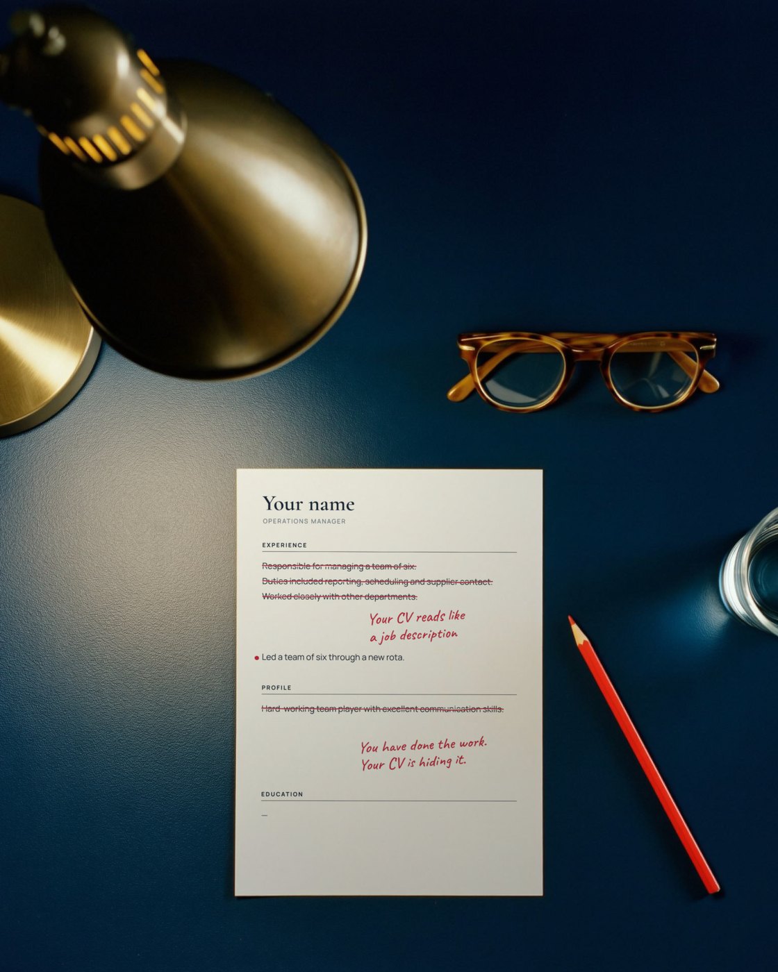 A CV marked up in red pencil under a desk lamp